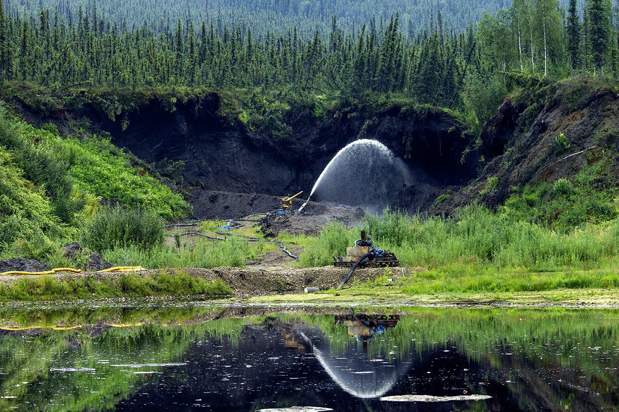 The giant monitor is spraying water onto the frozen muck and the permafrost is melting away at the Boneyard Alaska.. Placer mining for gold photo