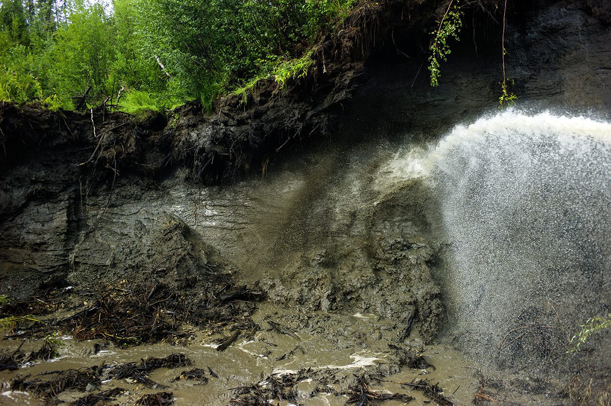 The giant monitor is spraying water onto the frozen muck and the permafrost is melting away at the Boneyard Alaska.. Placer mining for gold photo