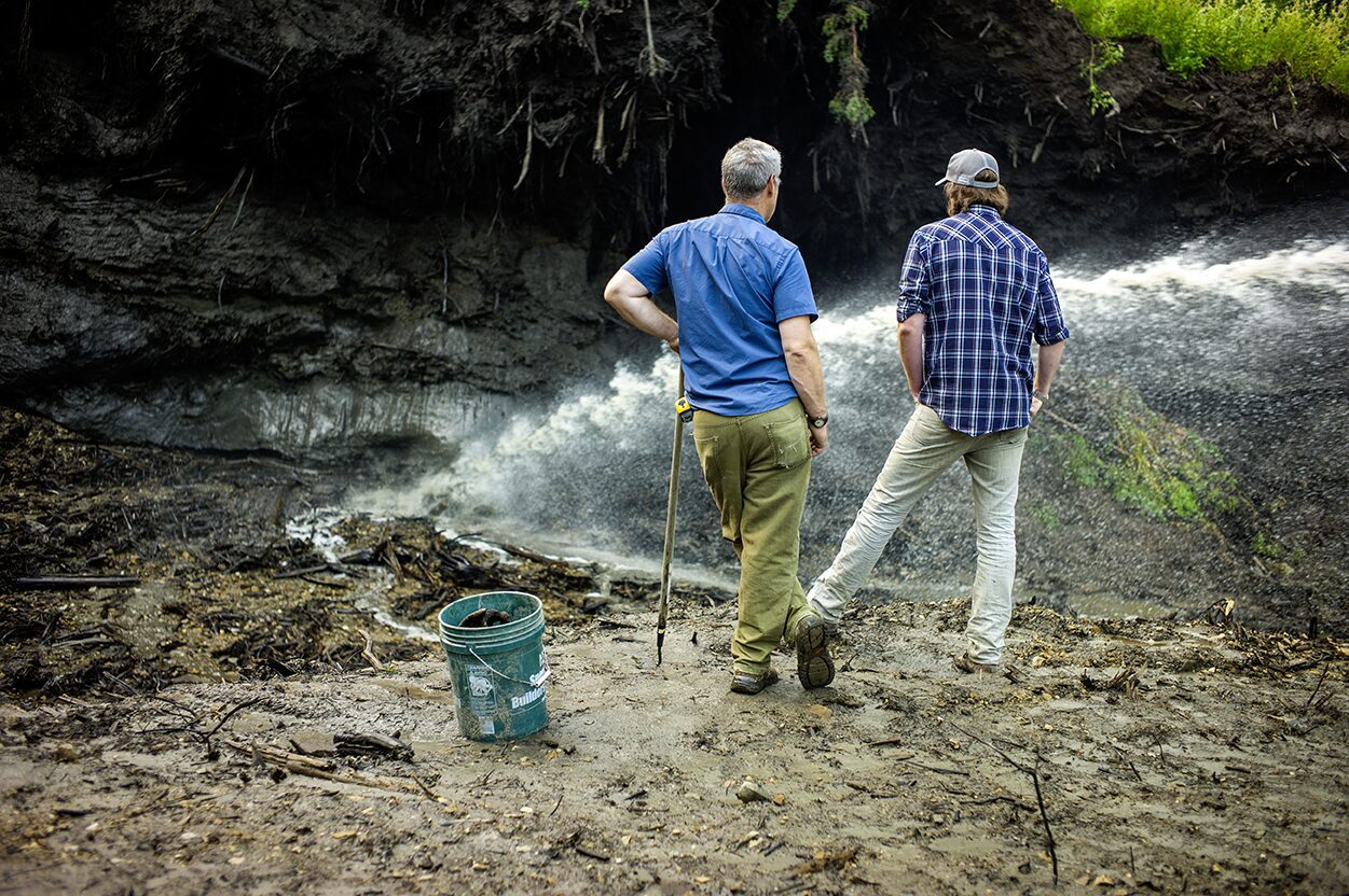Two man standing watching ice melt, permafrost ice melt as water is sprayed onto it.