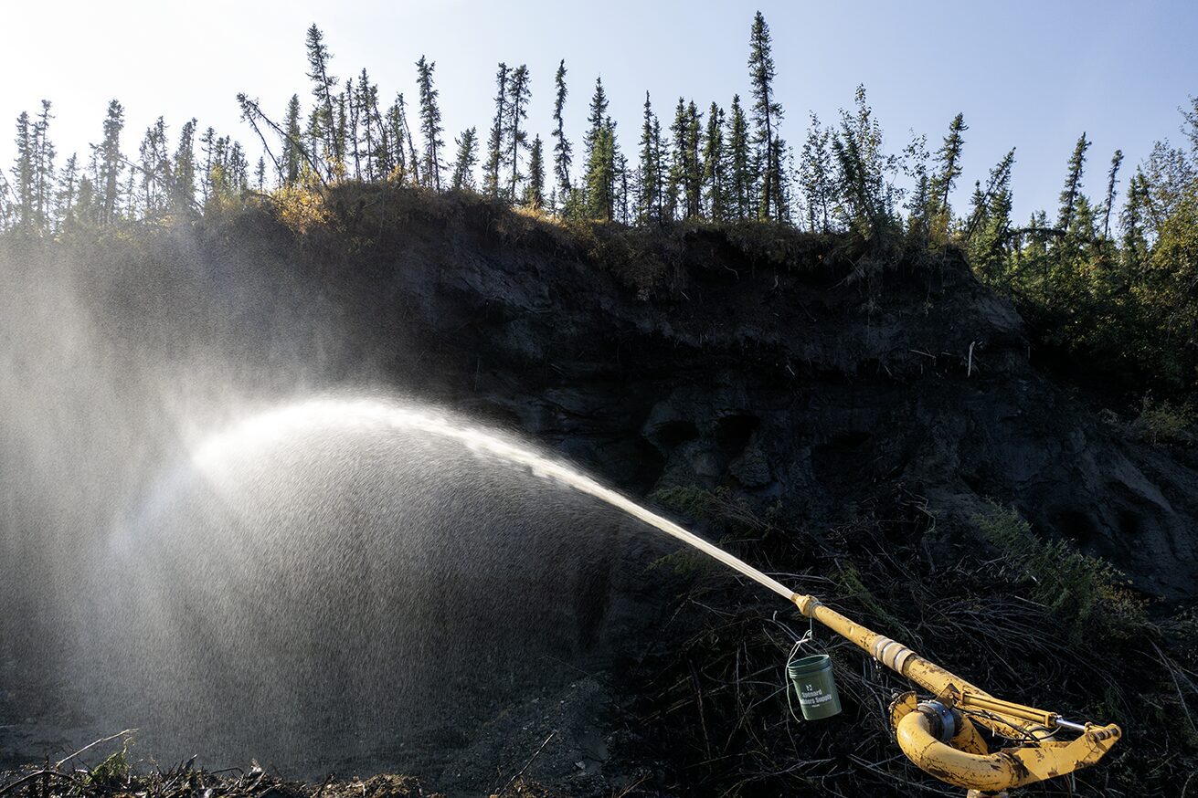 The giant monitor is spraying water onto the frozen muck and the permafrost is melting away at the Boneyard Alaska.. Placer mining for gold photo